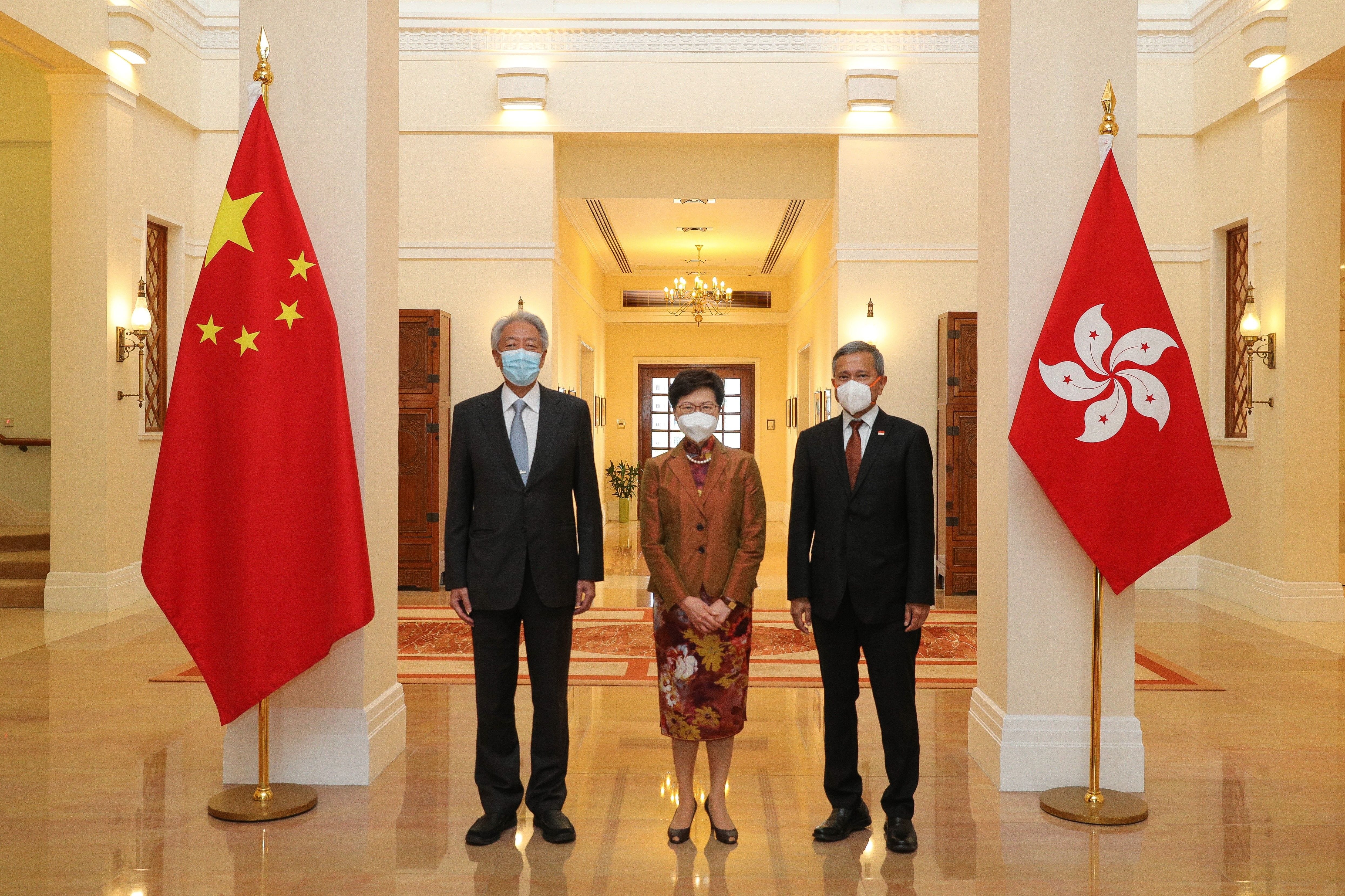 Two men and a woman wearing masks stand between the flags of China and Hong Kong.